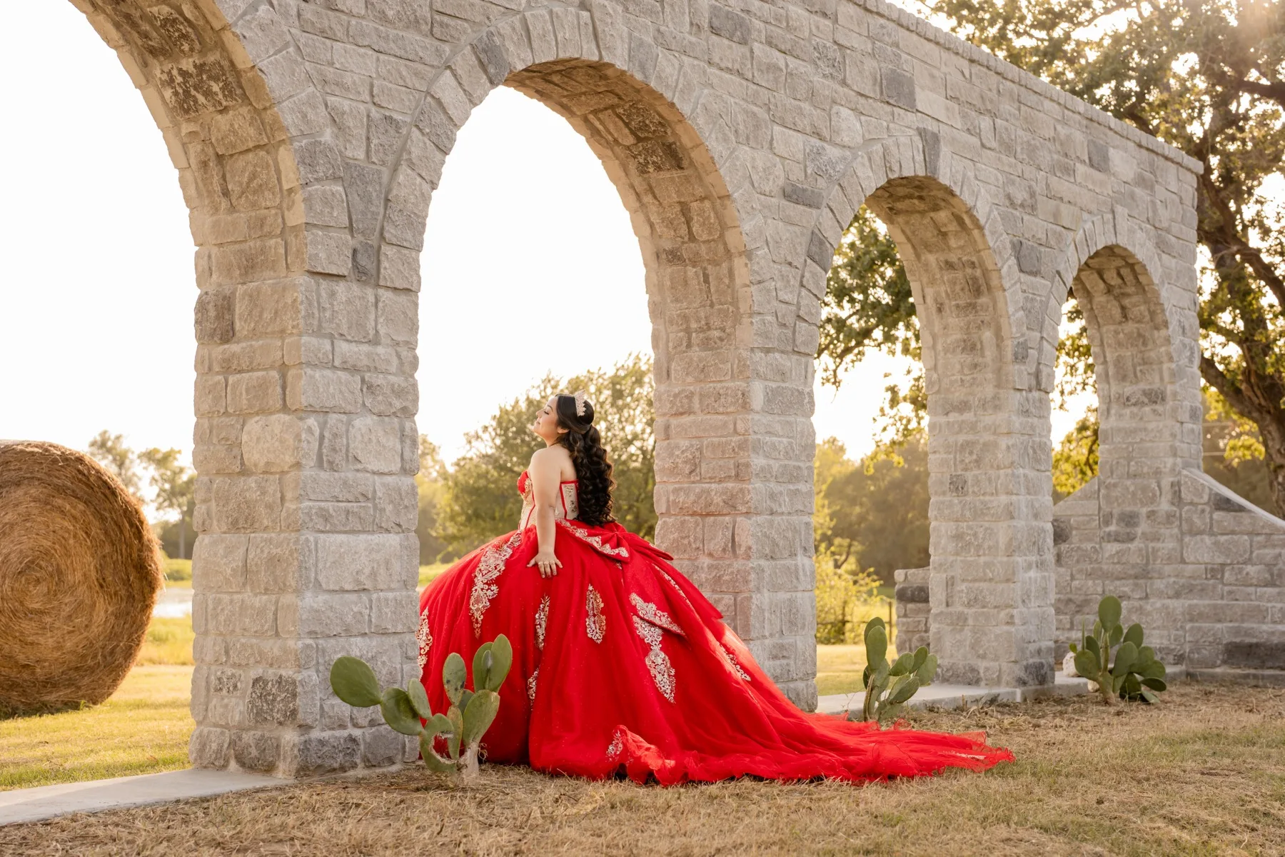 Quinceanera portrait in a red gown beside outdoor stone arches